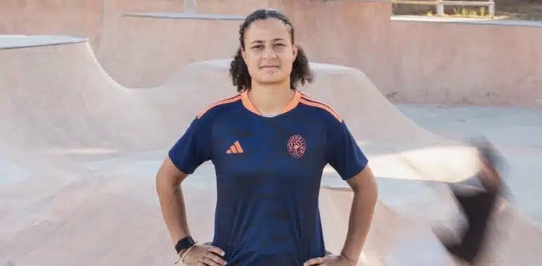 Screenshot | AllezPaillade.com Person standing with hands on hips in a skate park bowl, wearing a dark blue jersey with orange accents.