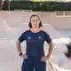 Person standing with hands on hips in a skate park bowl, wearing a dark blue jersey with orange accents.