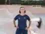 Person standing with hands on hips in a skate park bowl, wearing a dark blue jersey with orange accents.