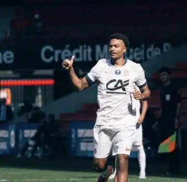 Soccer player in a white jersey and shorts runs on the field, giving a thumbs-up during a match.
