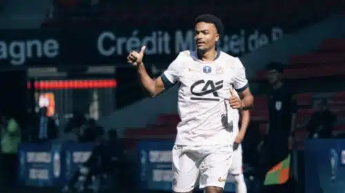 Soccer player in a white jersey and shorts runs on the field, giving a thumbs-up during a match.