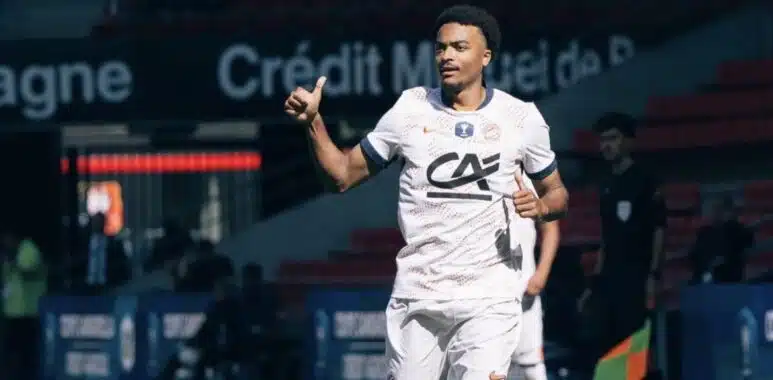 Screenshot | AllezPaillade.com Soccer player in a white jersey and shorts runs on the field, giving a thumbs-up during a match.