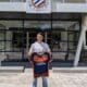 Young man standing outside a sports club entrance, holding a blue and orange team jersey.