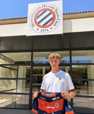 Screenshot | AllezPaillade.com Young man stands outside Montpellier Hérault Sport Club, holding a red-and-navy team jersey in front of the storefront sign.