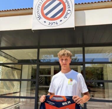 Young man stands outside Montpellier H&eacute;rault Sport Club, holding a red-and-navy team jersey in front of the storefront sign.