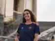 Smiling woman in a navy blue and orange sports jersey standing by stone stairs and railing outdoors.