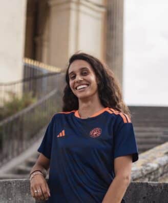 Smiling woman in a navy blue and orange sports jersey standing by stone stairs and railing outdoors.