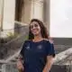 Smiling woman in a navy blue and orange sports jersey standing by stone stairs and railing outdoors.