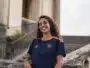Smiling woman in a navy blue and orange sports jersey standing by stone stairs and railing outdoors.