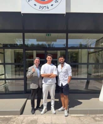 Screenshot | AllezPaillade.com Three men stand outside a glass-front building, smiling for the camera; left man in a gray blazer gives a thumbs up, middle in white outfit, right in white shirt and shorts.