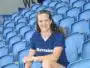 Smiling woman sitting in blue stadium seats, wearing a navy T-shirt with 'Havraise' logo.
