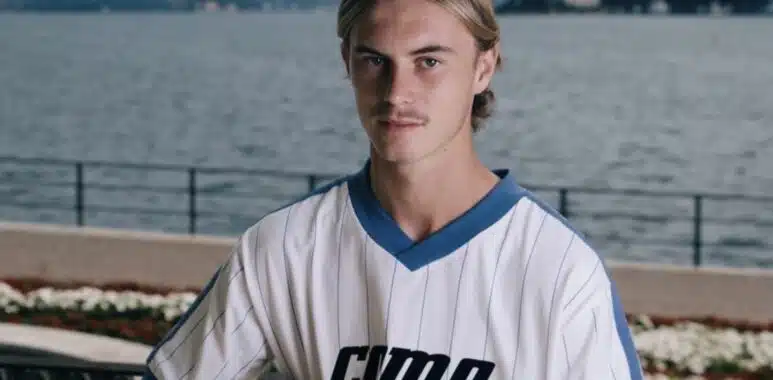 Screenshot | AllezPaillade.com Young man in a white pinstriped soccer jersey holds a ball, posing by a lakeside with mountains in the background
