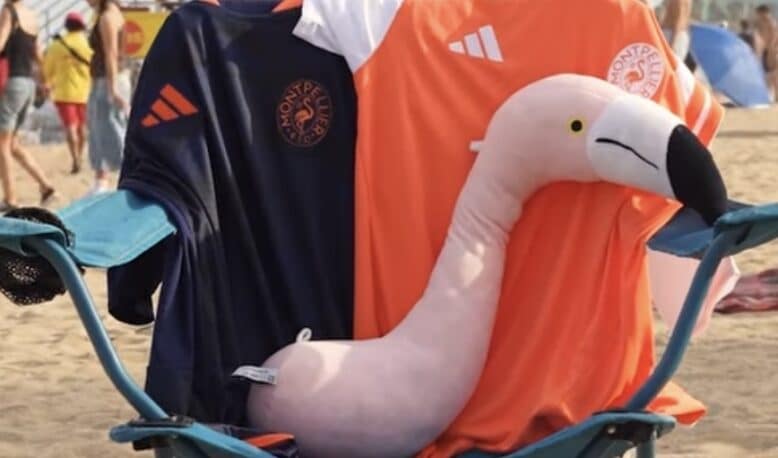 Screenshot | AllezPaillade.com Pink inflatable flamingo resting on a blue beach chair, draped with dark blue and orange towels bearing logos.