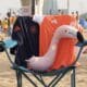 Pink inflatable flamingo resting on a blue beach chair, draped with dark blue and orange towels bearing logos.