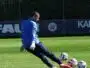 Soccer goalkeeper in blue jersey and white gloves kicking multiple balls on a green field.