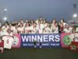 Girls soccer team posing with trophies after winning, holding a banner that reads WINNERS at a stadium during sunset.