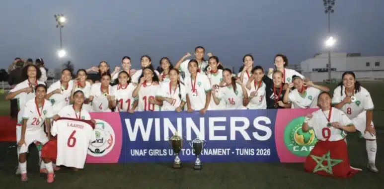 Screenshot | AllezPaillade.com Girls soccer team posing with trophies after winning, holding a banner that reads WINNERS at a stadium during sunset.