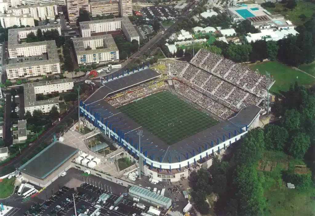 MOSSON_02 | AllezPaillade.com Aerial view of a large sports stadium with crowded stands, green playing field, and surrounding city blocks and trees.