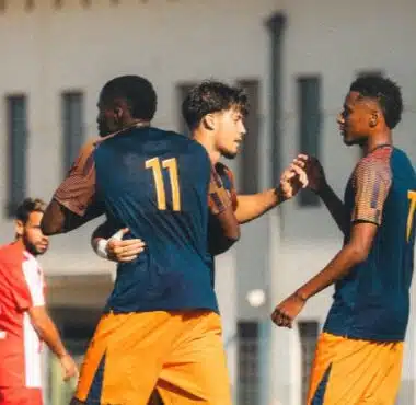 Two soccer players celebrate together on the field, wearing blue jerseys and orange shorts, with the number 11 on one player's back.