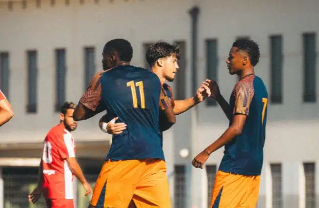 Two soccer players celebrate together on the field, wearing blue jerseys and orange shorts, with the number 11 on one player's back.