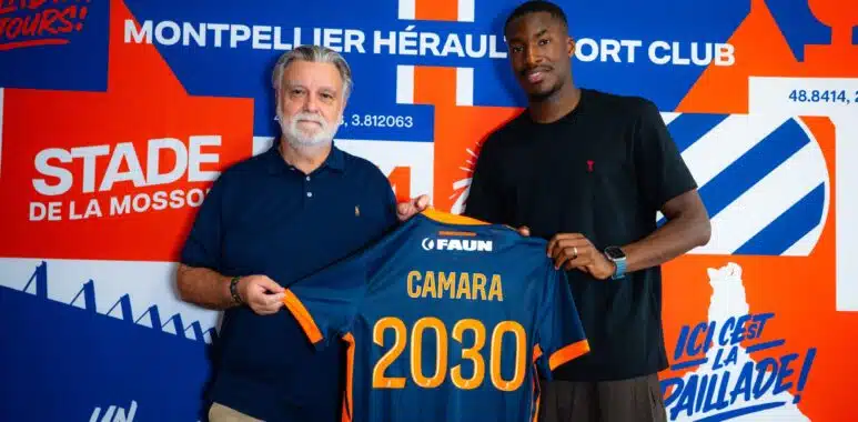 camara | AllezPaillade.com Two men pose together, one older with a blue polo and the other in a black shirt, holding a blue-and-orange jersey in front of a bold blue-orange mural.