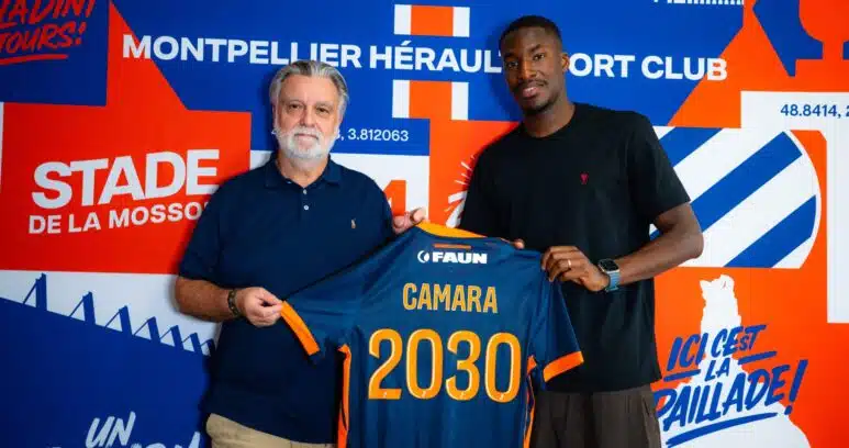 camara | AllezPaillade.com Two men pose together, one older with a blue polo and the other in a black shirt, holding a blue-and-orange jersey in front of a bold blue-orange mural.