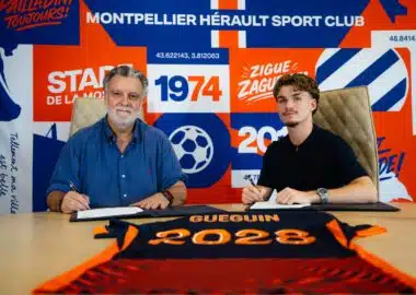 Two men sit at a table, signing documents, with a bright blue and orange sports club backdrop behind them.