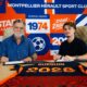 Two men sit at a table, signing documents, with a bright blue and orange sports club backdrop behind them.