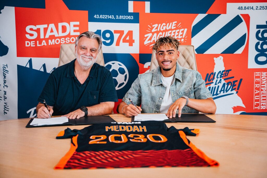 dsc00175-2048x1365 | AllezPaillade.com Two men sit at a table signing documents, with a bright graphic wall behind them.",