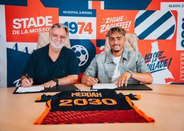 dsc00175-2048x1365 | AllezPaillade.com Two men sit at a table signing documents, with a bright graphic wall behind them.",
