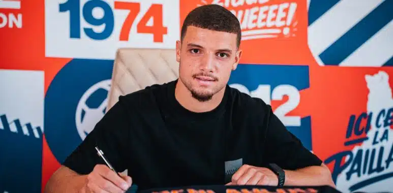 dsc01105-2048x1365 | AllezPaillade.com Man signing autographs at a table in front of a bright orange and blue backdrop with logos.