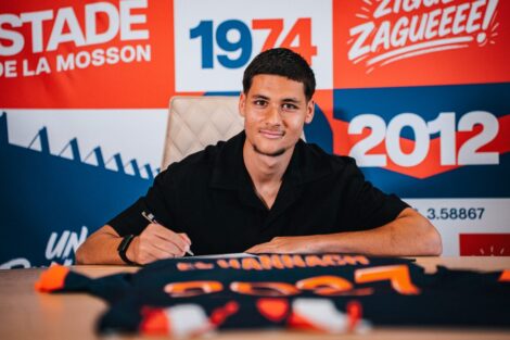 Young man signs a document at a table, with a bright red and blue graphic backdrop behind him.