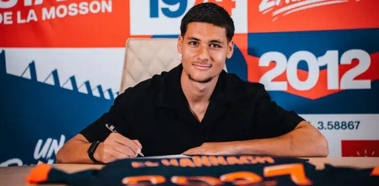 Young man signs a document at a table, with a bright red and blue graphic backdrop behind him.