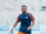 Male soccer player in a blue training shirt and orange shorts on a blurred stadium field, mid-action pose.
