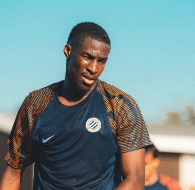 Male soccer player in a dark blue training jersey on a sunny day, focused during practice.