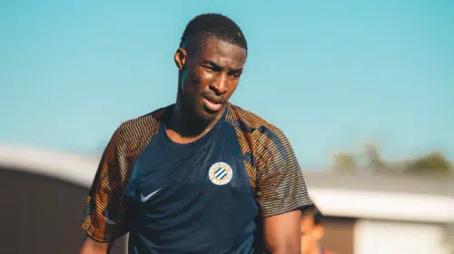 Male soccer player in a dark blue training jersey on a sunny day, focused during practice.