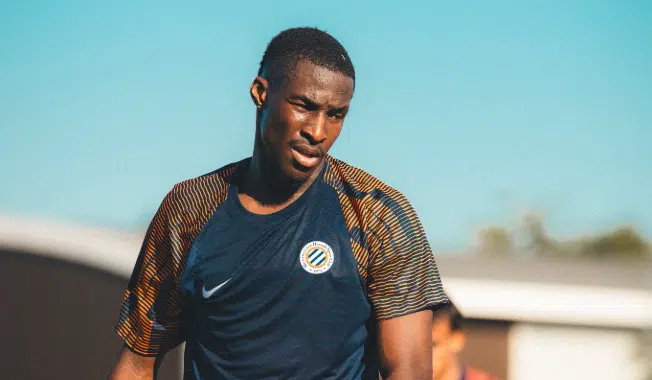 Male soccer player in a dark blue training jersey on a sunny day, focused during practice.