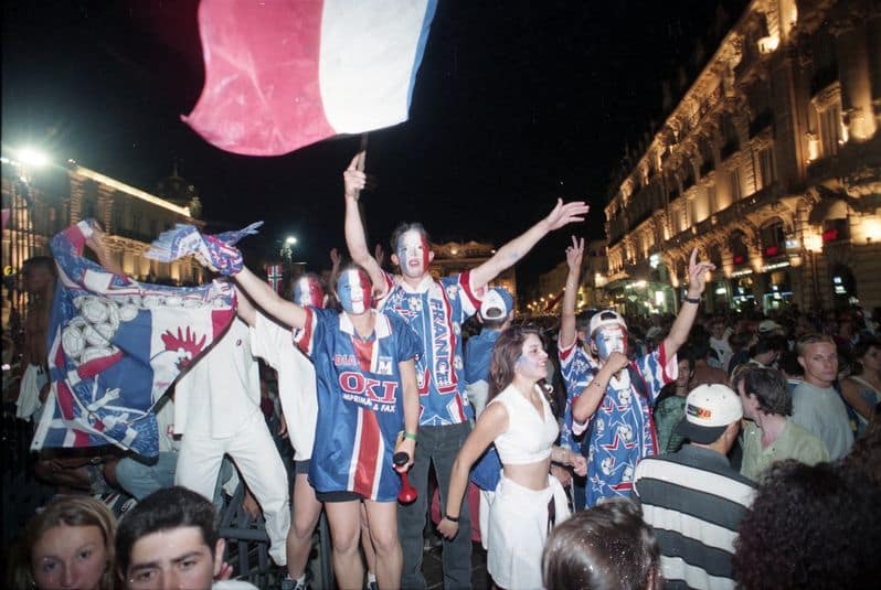 JMMAR20180606 | AllezPaillade.com Group of fans at a nocturnal parade, with face paint and red‑white‑blue outfits, waving a large flag.