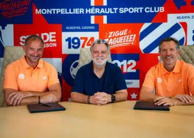 nicollin lefèvre maraval | AllezPaillade.com Three men sit at a table in front of a bright, graphic backdrop; left and right wear orange polo shirts while the center wears a dark blue shirt, posing for a team photo in front of a sports-club banner.