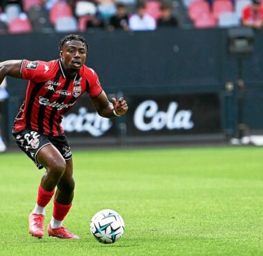 Soccer player in red-and-black stripes dribbles the ball on a green field during a match.