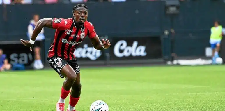 Soccer player in red-and-black stripes dribbles the ball on a green field during a match.