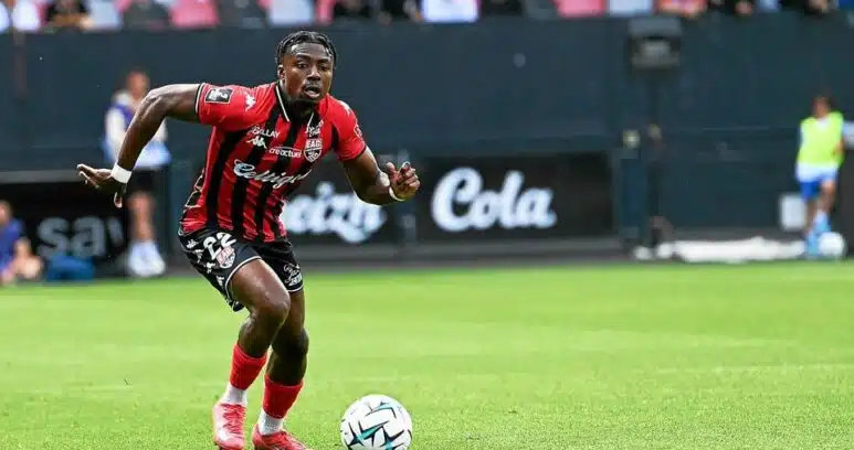 Soccer player in red-and-black stripes dribbles the ball on a green field during a match.