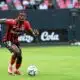 Soccer player in red-and-black stripes dribbles the ball on a green field during a match.