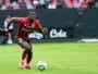 Soccer player in red-and-black stripes dribbles the ball on a green field during a match.