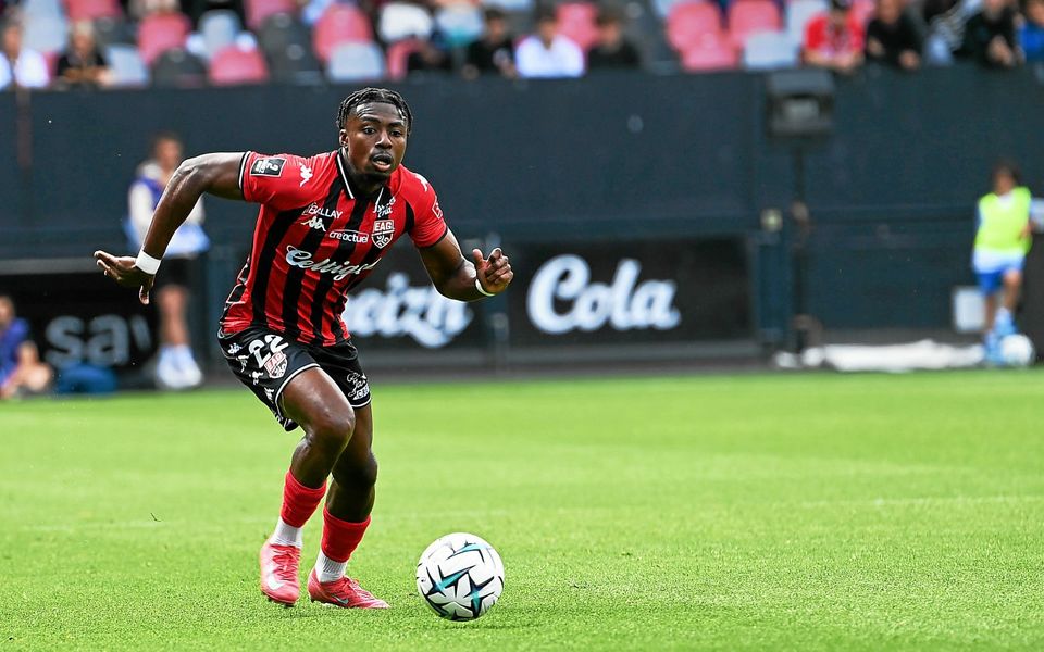 697b9733502bfcfcf10192d2 | AllezPaillade.com Soccer player in red-and-black stripes dribbles the ball on a green field during a match.