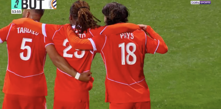Capture décran 2026-08-21 à 222249 | AllezPaillade.com Three soccer players in red uniforms hug on a green pitch; jersey numbers 5 and 18 visible, with 'PAYS' on one back—celebration moment during a match.