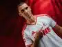 Portrait of a man in a white and red soccer jersey pointing to the team crest on his chest.