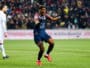 Soccer player in a navy kit (#23) celebrates a goal on a green field as teammates and fans cheer in the background.