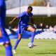 Soccer player in blue jersey controlling a ball on a grassy field with teammates and spectators in the background