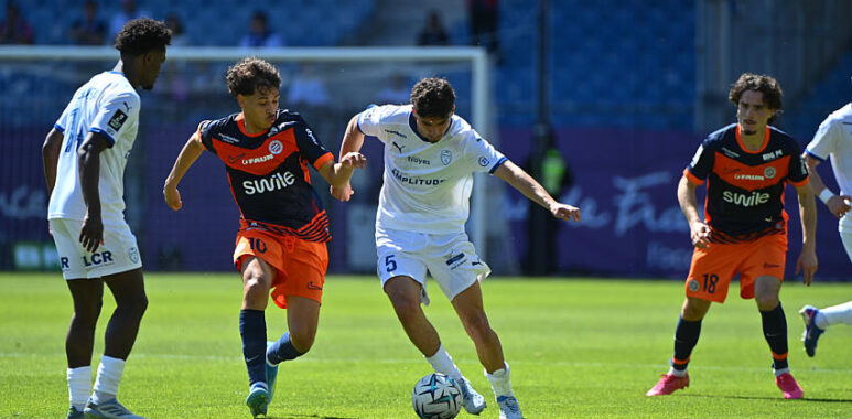 Fayad Pays | AllezPaillade.com Soccer players in white and orange kits contesting the ball on a sunny pitch near the goal.